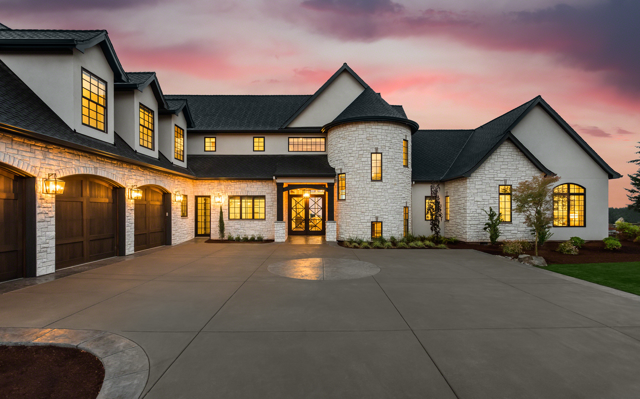 Stunning luxury home exterior at sunset new luxury home with three car garage, large driveway and glowing exterior and interior lights